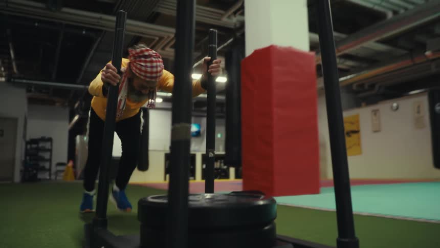 Man pushes a weight sled across the floor of an empty gym