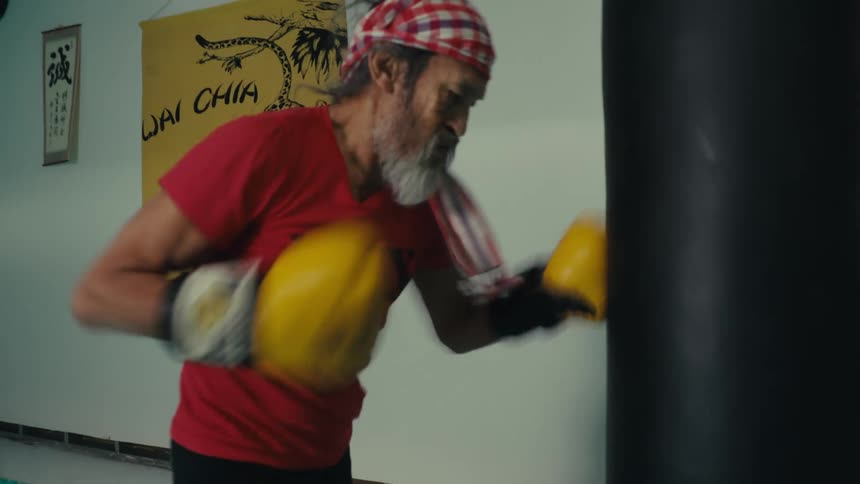 An older man punches a hanging bag in a gym