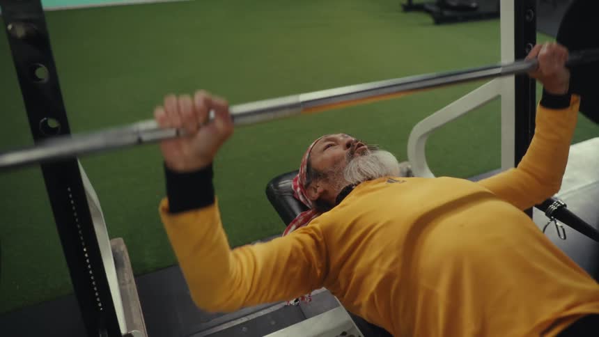An older asian man lifts weights in a gym