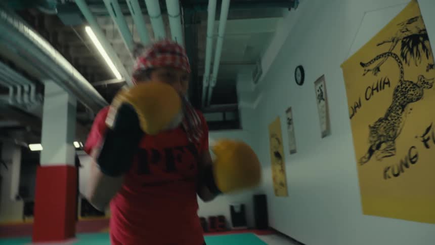 Concentrated white bearded man wearing yellow gloves and punching a punching bag