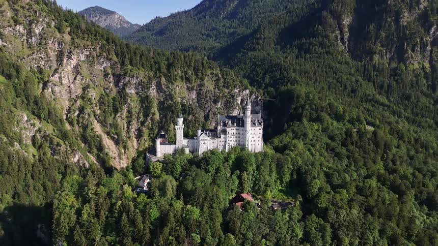 A large white castle amidst a forest of green trees in a mountainous region