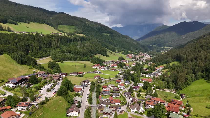 Aerial panorama of a village nestled in a green valley with mountains in the background under a partly cloudy sky