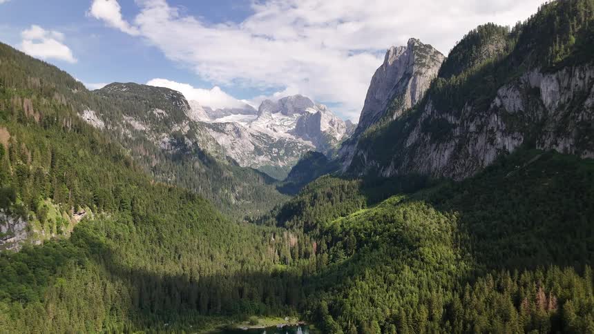 Forest surrounds a lake in a narrow valley in a mountain range under a cloudy sky