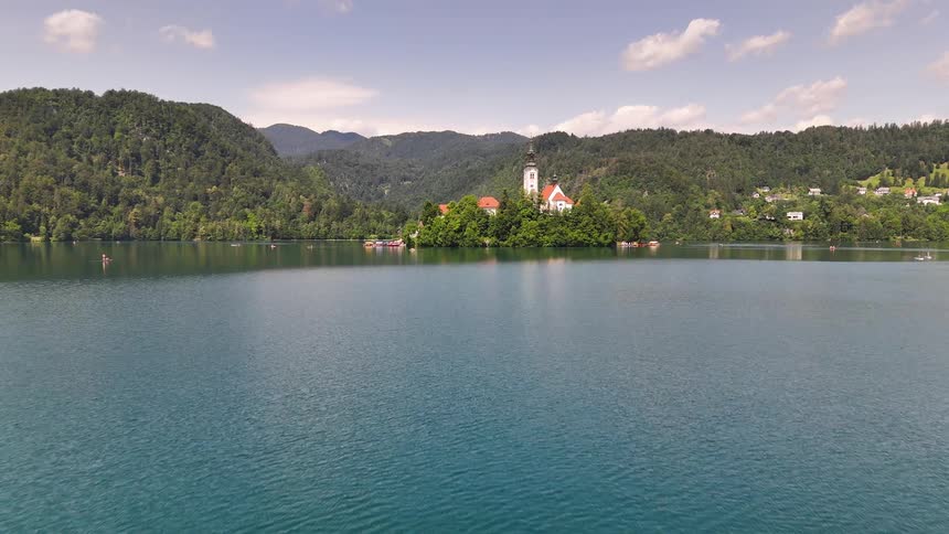 People in a small boat in the middle of a serene lake with a wooded island in the background where a picturesque church stands out