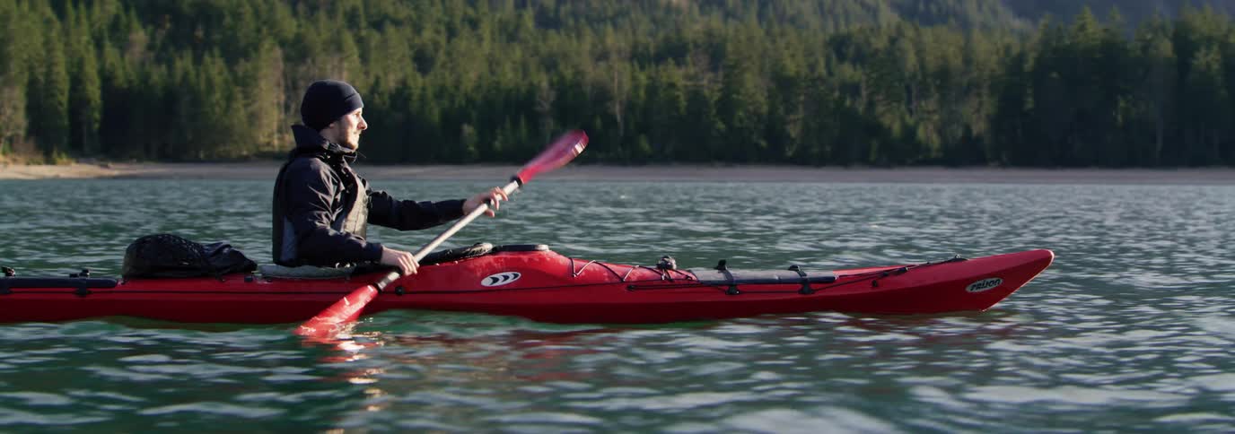 An man kayaking on a serene body of water surrounded by a forested landscape