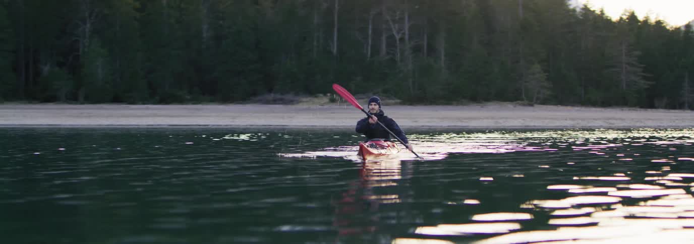 Man kayaking in the middle of a lake in front of an evergreen forest
