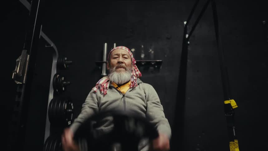 Concentrated elderly man doing weightlifting with a weight plate