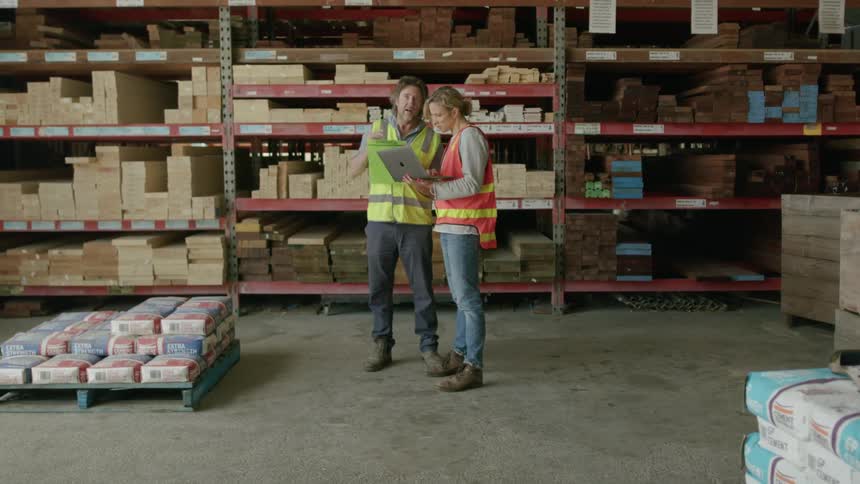 Two coworkers look at a laptop in the lumber yard