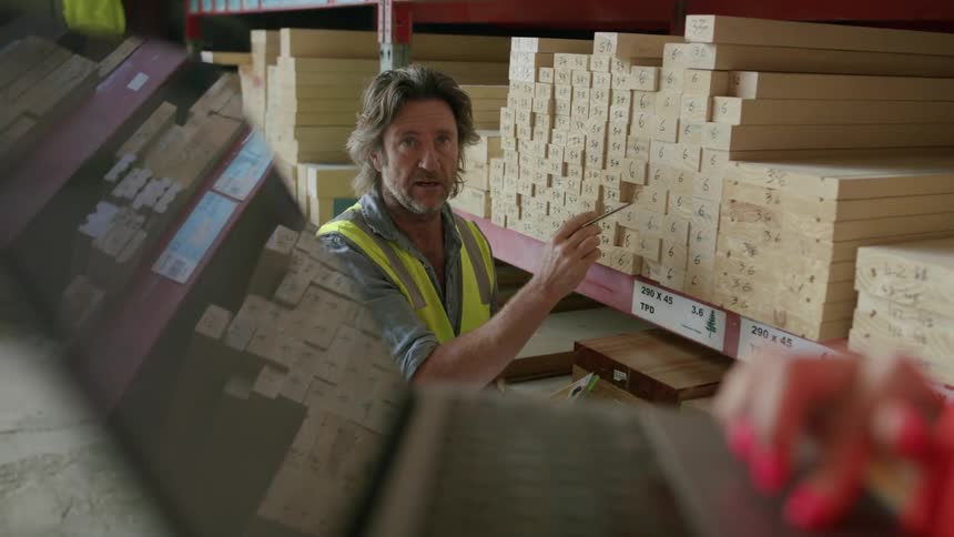 Woman inputs information man is telling her while he examines wood on the shelves