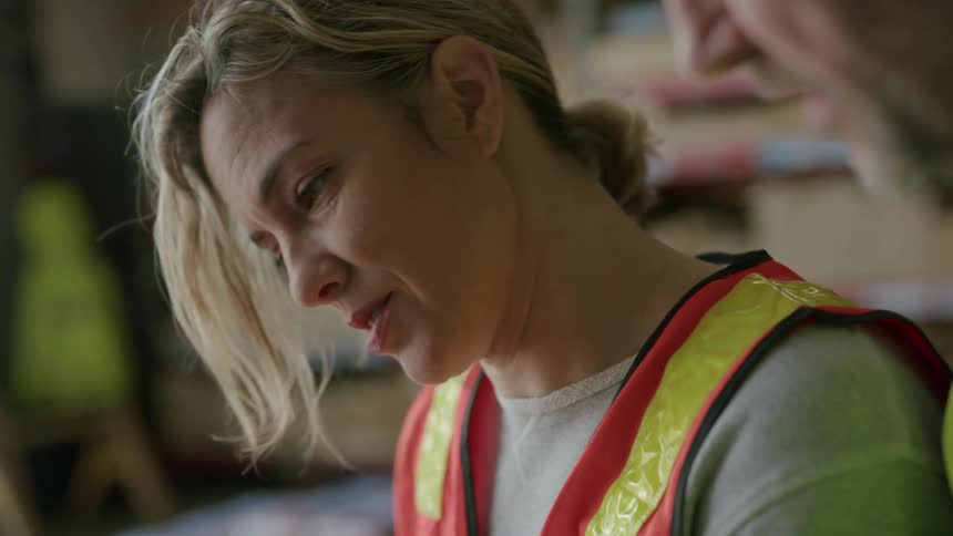 Woman sitting wearing a signaling vest talking to a colleague next to her