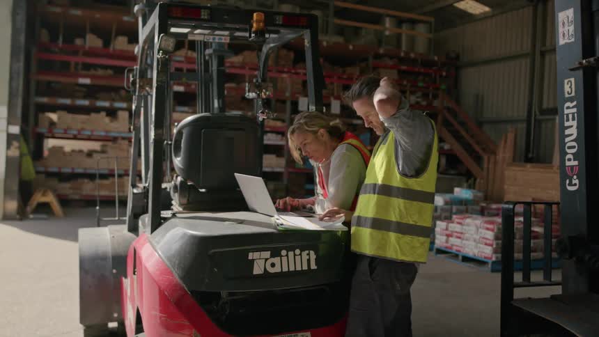 Coworkers in a warehouse working on paper and a laptop