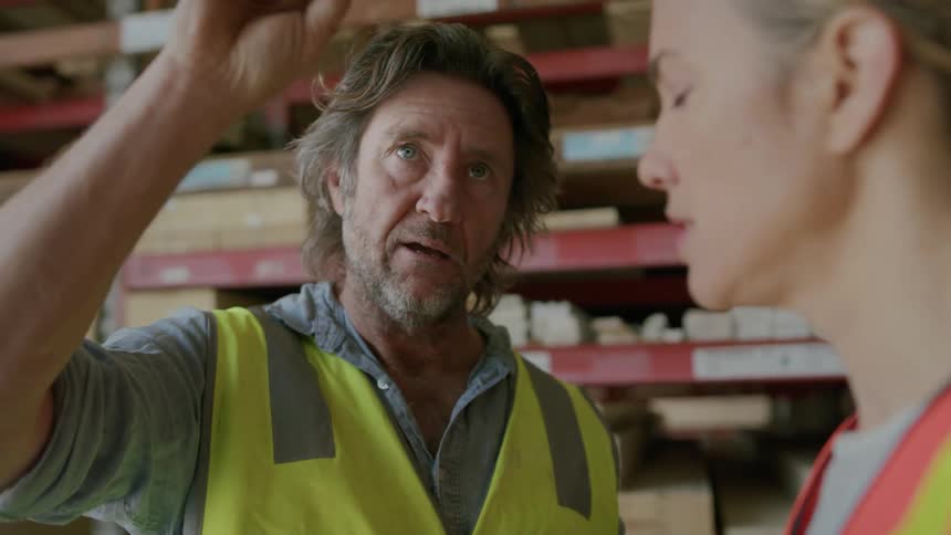 Two workers have a discussion while one of them uses a laptop