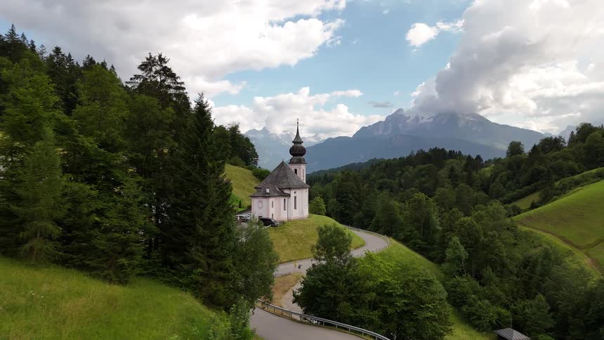 A white church with a tower with cross on top in a region with a green hills and forest of trees