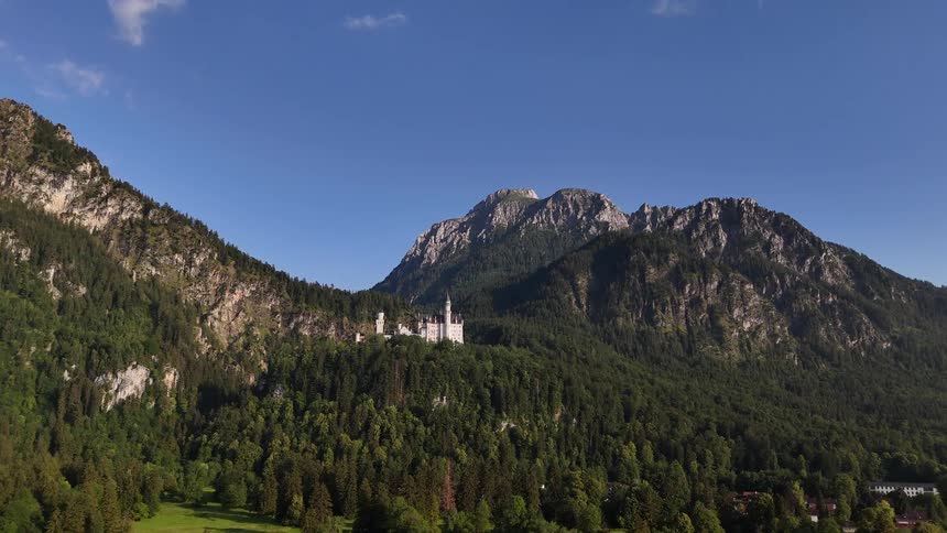 Castle standing on forested mountain slope towers over rural countryside on a slightly cloudy day