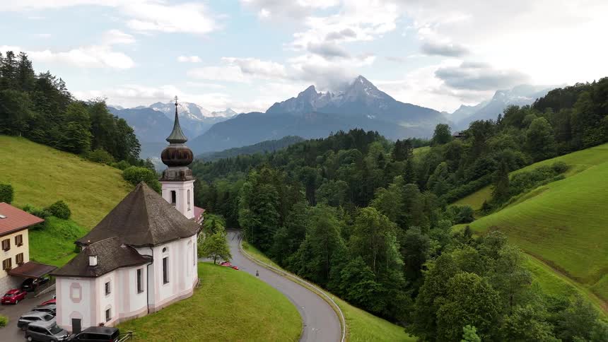 A church and other buildings sit on a slope near a forest