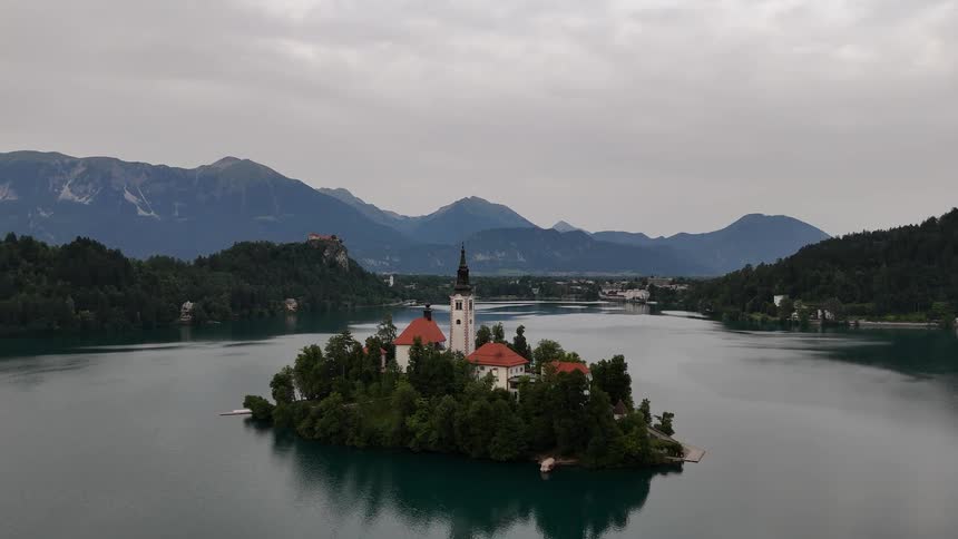 A castle sits on an island in a lake surrounded by mountains and forests