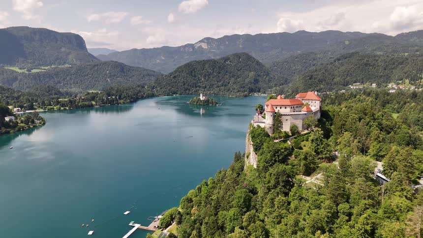 Red roofed keep stands on a forested mountain overlooking the lake on a foggy day