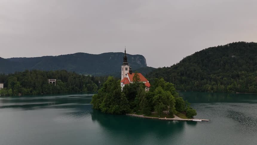 A large building sits on a forested island in the middle of a lake
