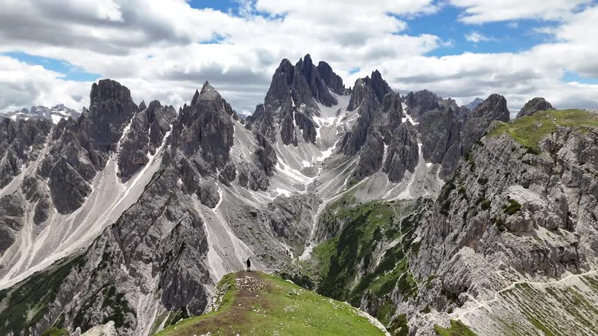 A person stands on the top of a mountain looking at the massive mountain ranges nearby