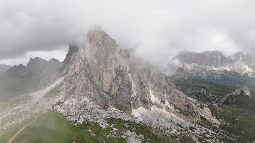 A huge stone mountain in a mountain range where there is cloud on top of the mountains