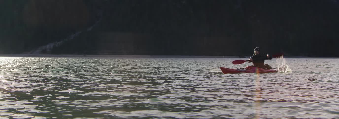 A man is in a red kayak on a river and using a red paddle to move