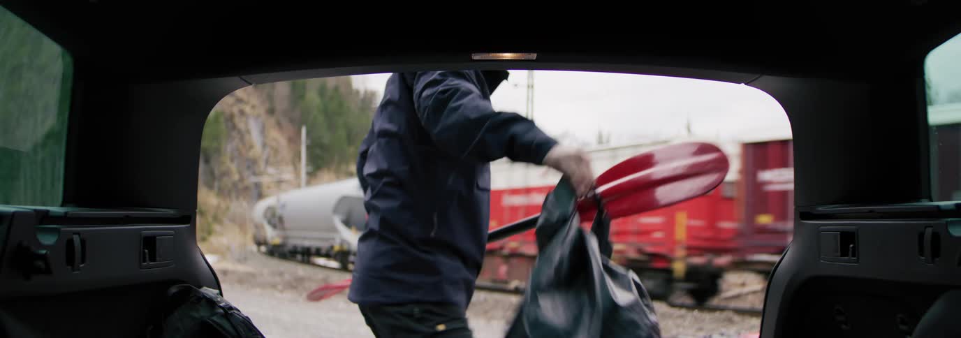 A man removes a paddle and a bag from the trunk of a car and places the paddle inside the canoe