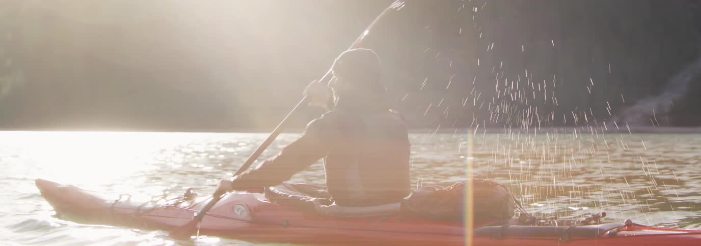 Man paddling a red kayak on a lake at sunset
