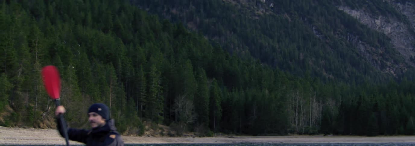 Man paddling a red kayak on a calm body of water with mountains in the background