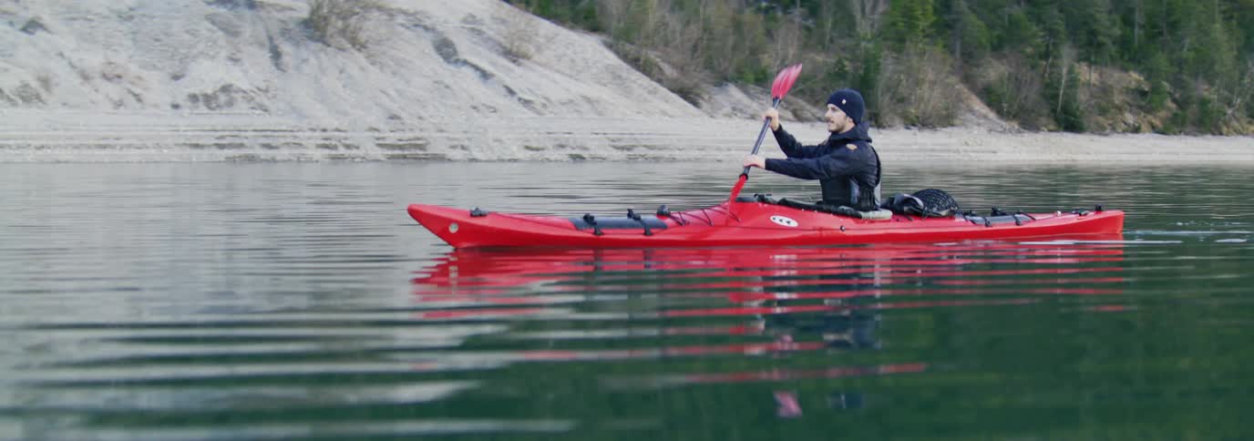 Man paddling a red kayak on lake