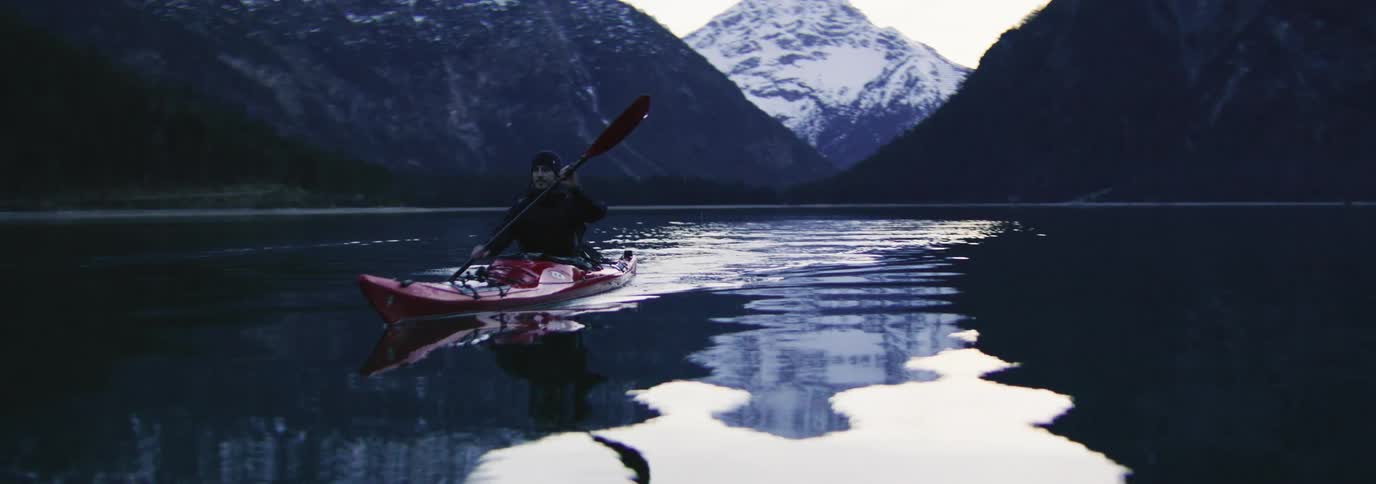 Man paddling a kayak in calm waters with mountains in the background