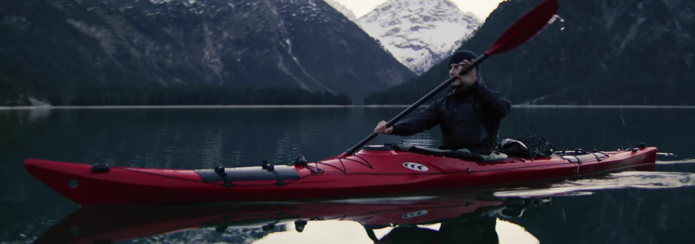 Man paddling a red kayak in calm waters of a reflective lake