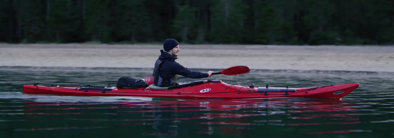 An individual kayaking on calm waters with a forest in the background