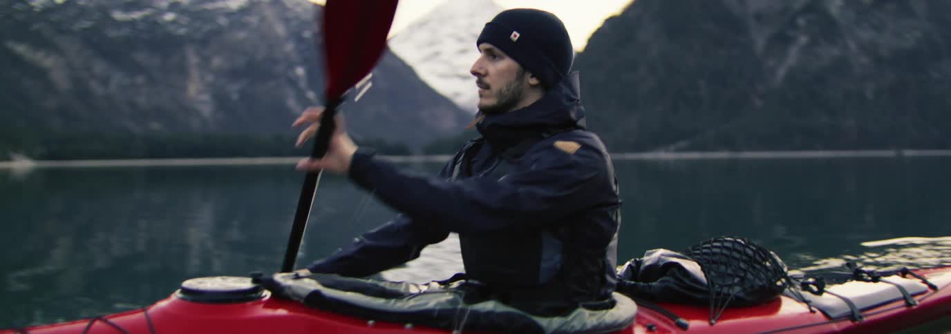 Man paddling a red kayak in calm waters with mountains in the background