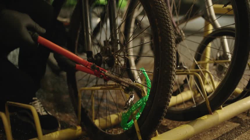 A man wearing gloves cuts a chain in order to steal a bicycle