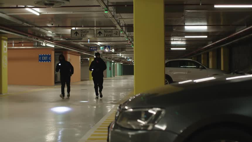 You are hooded men in black clothes running with flashlights in a parking lot of a building