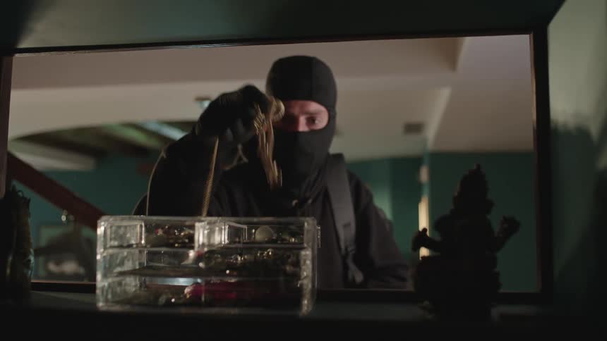 Two men wearing balaclavas enter a house and take objects from a shelf and then go up the stairs