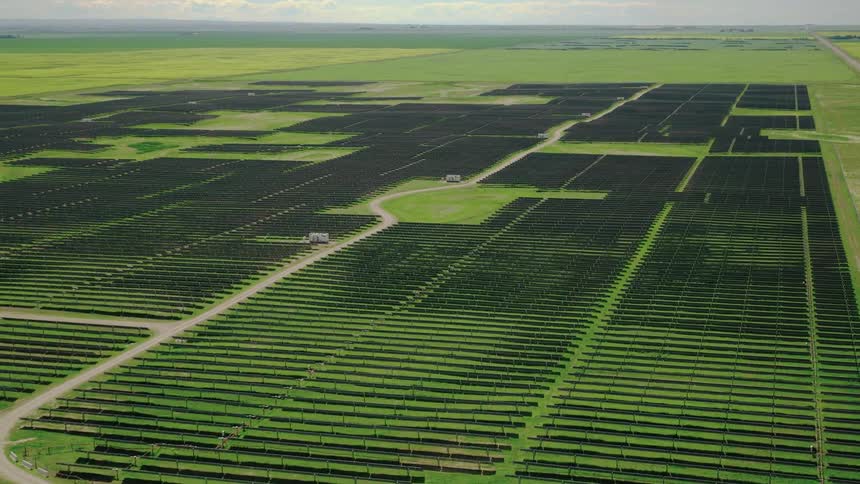 A large solar farm with rows of photovoltaic panels covering a vast green field