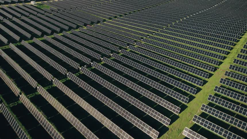 Aerial view of a vast solar farm with numerous rows of photovoltaic panels stretching across a green landscape