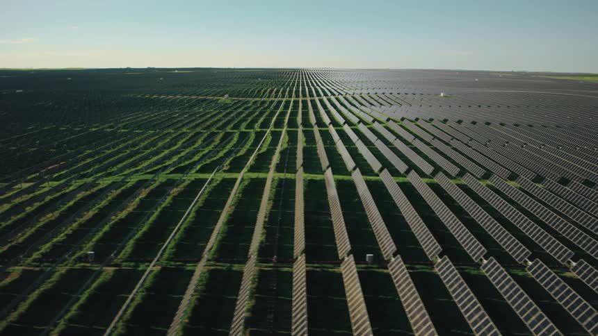 Aerial view of a vast solar farm with numerous rows of photovoltaic panels stretching across a green landscape