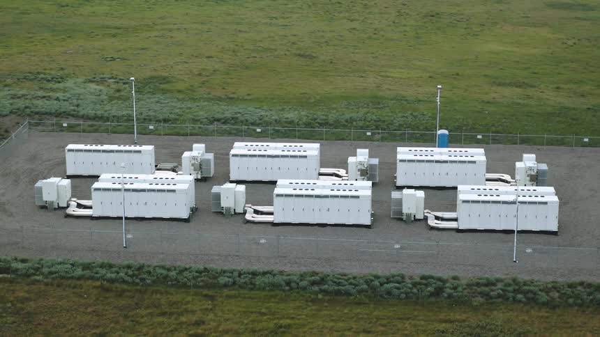 Aerial view of a fenced facility with large white industrial battery units prioviding grid backup