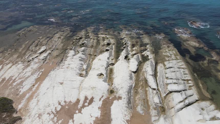 An aerial view of a coastal area with white chalk cliffs and rock formations extending into a clear blue sea