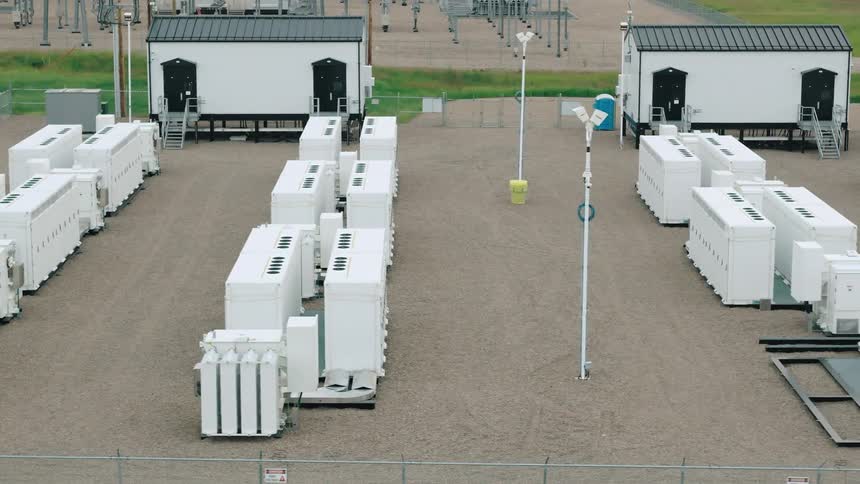 Aerial view of a fenced facility with large white batteries arranged in rows