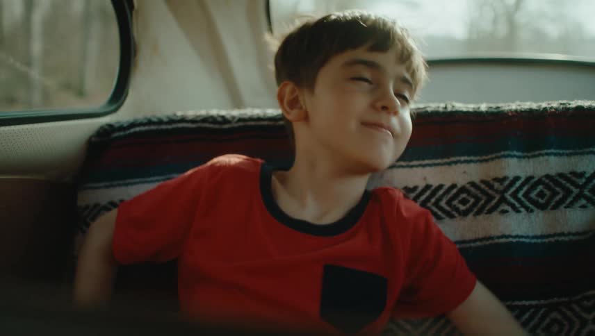 A boy in a red shirt is sitting in the back seat of a moving car