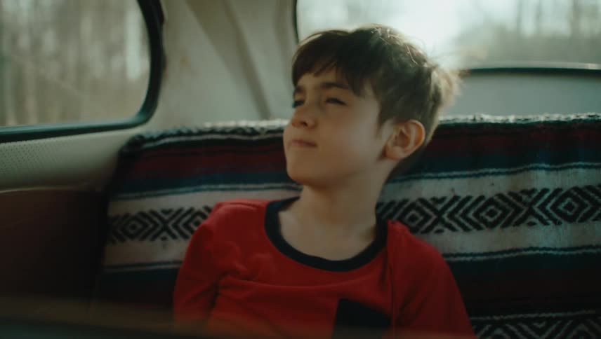 A boy is riding in the backseat of the car