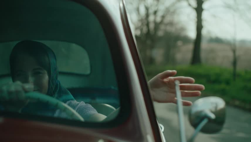 A woman with a headscarf is driving a car and has her hand out the window