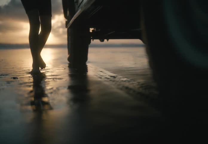 Barefoot child walks across wet sand to a vehicle parked on the beach near sunrise