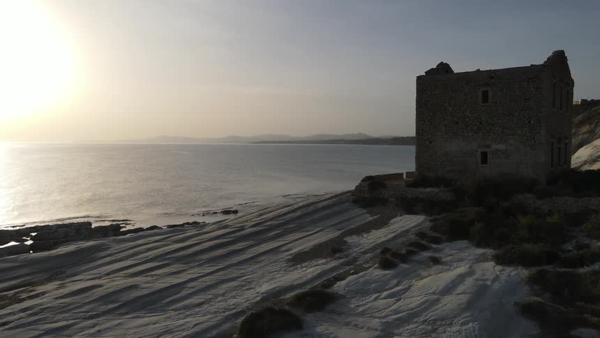 Lone stone structure in a coastal landscape with the sun low on the horizon