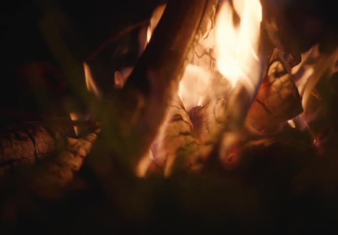 Closeup of a campfire in the dark burning brightly with orange and yellow flames licking upwards