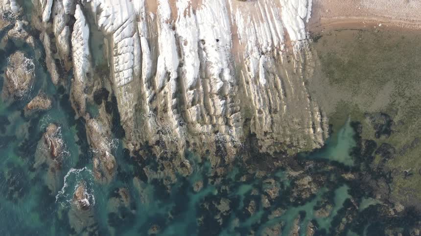 Coastal scenery with steep cliffs meets a body of water with different shades of blue and green