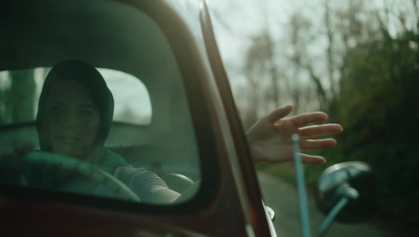 Smiling woman driving a classic vehicle with one hand out the window